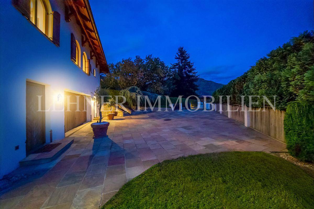 Großer gepflasterter Vorplatz mit Garagenzugang und Beleuchtung bei Einbruch der Dunkelheit.