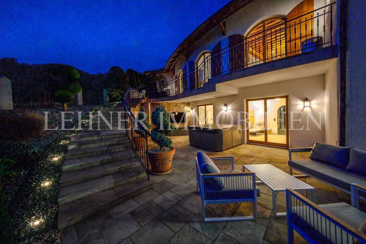 Gemütliche Terrasse mit Sitzgelegenheiten und Whirlpool, umgeben von beleuchteten Stufen und Natursteinmauern.