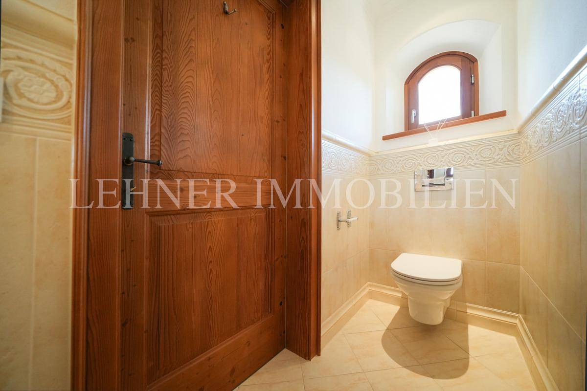 Gäste-WC mit Wand-WC, Holztür und kleinem Fenster, in beigen Farbtönen.