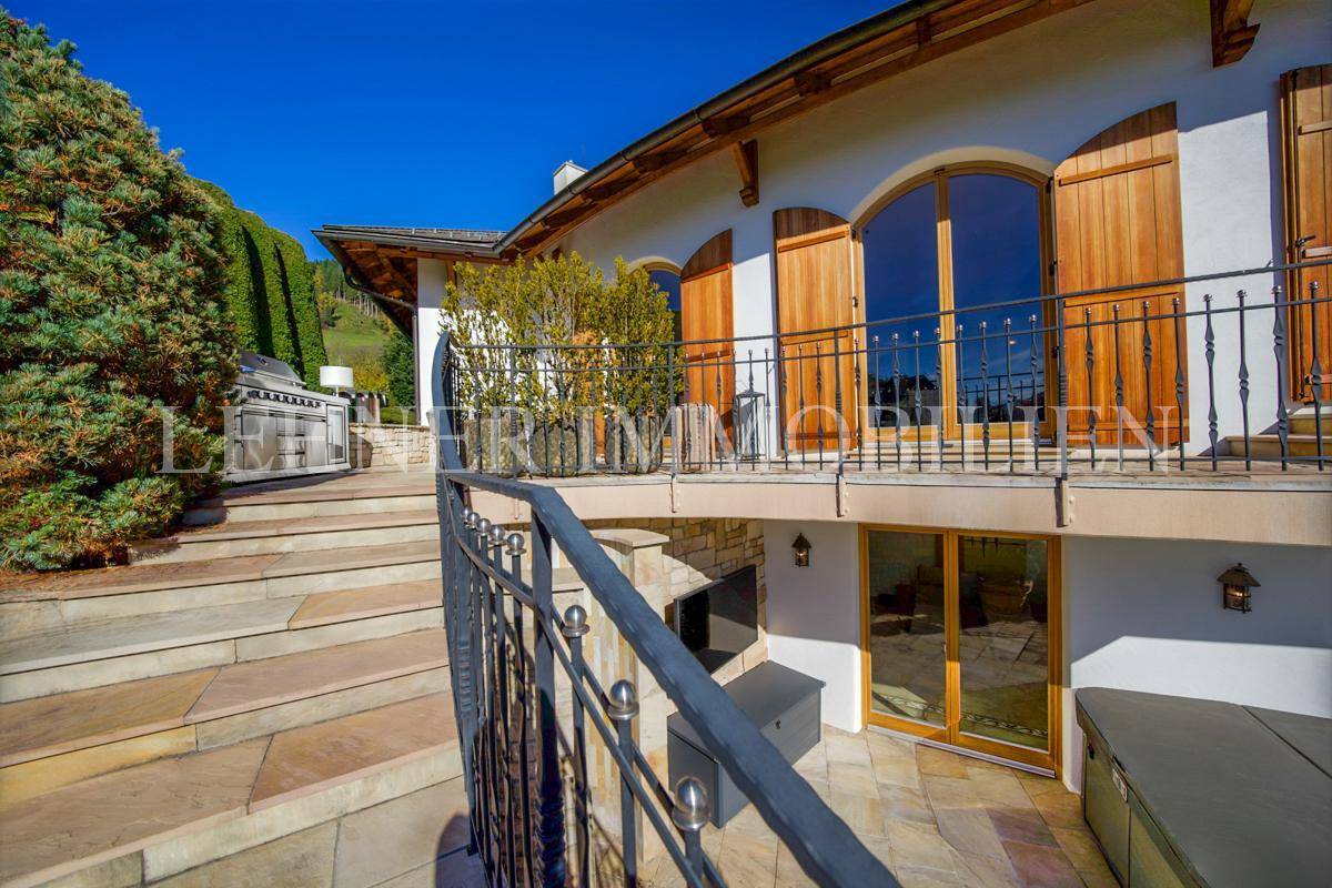 Balkon mit Holztüren und schmiedeeisernem Geländer, darunter ein Terrassenbereich.