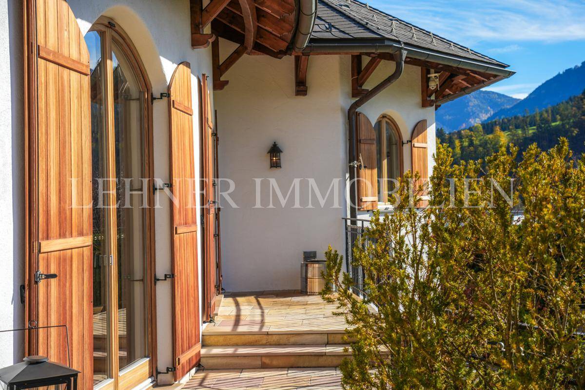 Balkon mit Holztüren und schmiedeeisernem Geländer, umgeben von üppiger Vegetation.