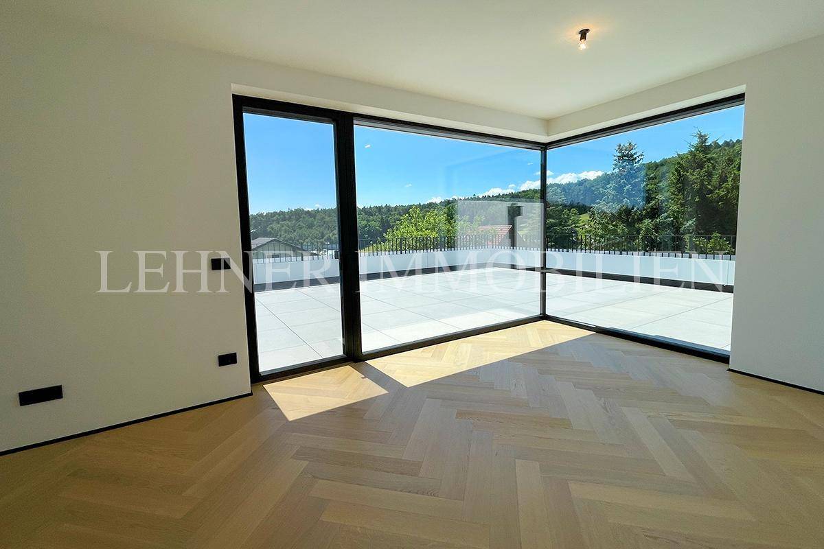 Heller Raum mit Fischgrätparkett und raumhohen Fenstern mit Zugang zur Dachterrasse.