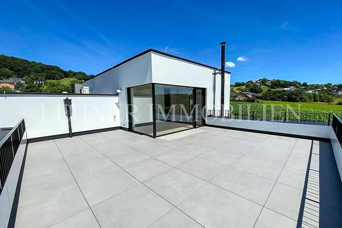 Sonnige Dachterrasse mit Fliesenboden und weitem Blick auf die grüne Umgebung.
