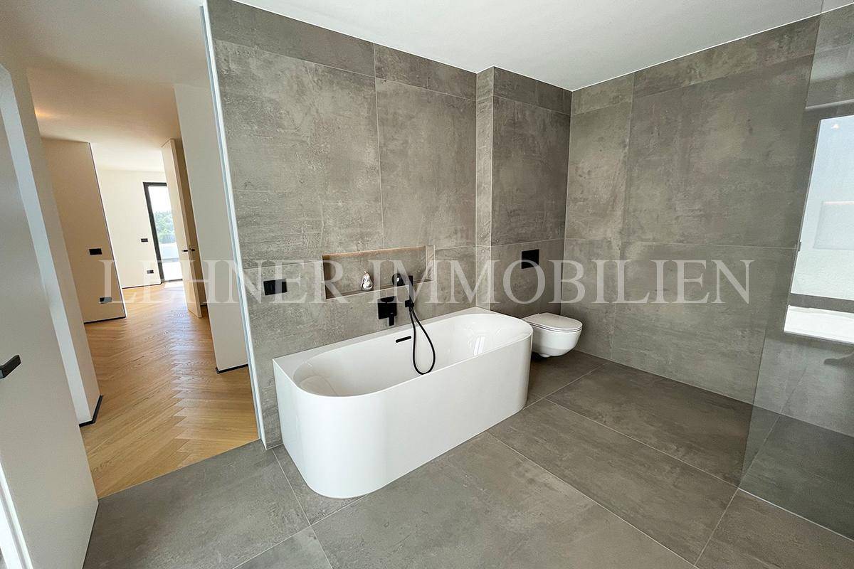 Geräumiges Badezimmer mit freistehender Badewanne, Wand-WC und grauen Fliesen.