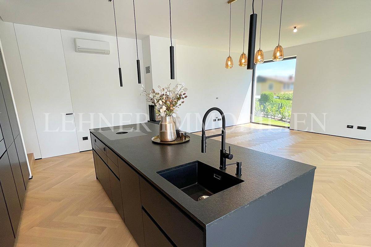 Elegante schwarze Kücheninsel mit Spüle und modernen Hängelampen in einem hellen Raum.