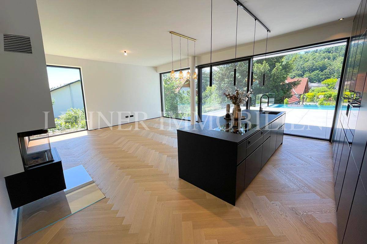 Offener Wohnbereich mit moderner schwarzer Küche, Fischgrätparkett und großen Panoramafenstern.