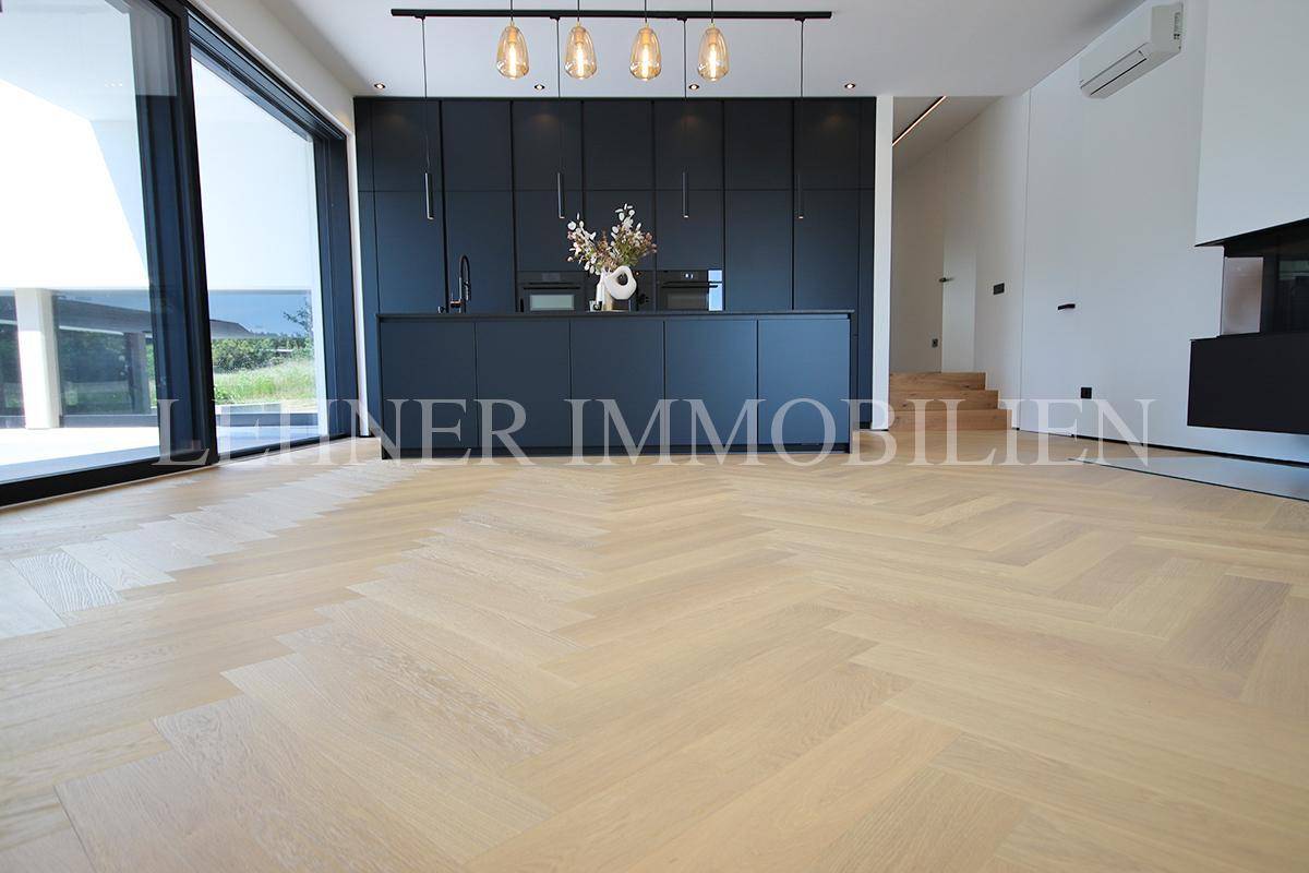 Offener Wohnbereich mit Fischgrätparkett und moderner schwarzer Einbauküche.