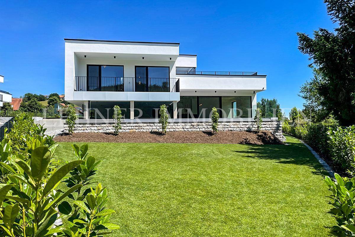 Moderne Villa mit weitläufigem Rasen und Blick auf die umliegende Natur.