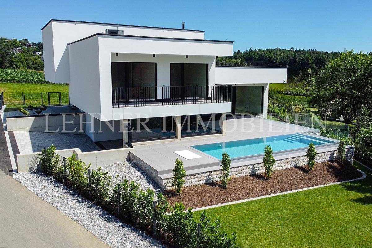 Moderne Villa mit Pool und gepflegtem Garten, umgeben von grüner Landschaft.