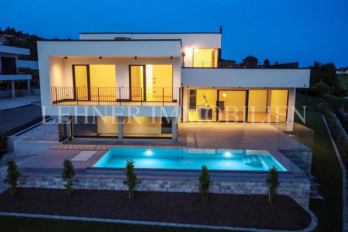 Elegante moderne Villa mit beleuchtetem Pool und gepflegtem Gartenbereich in der Dämmerung.