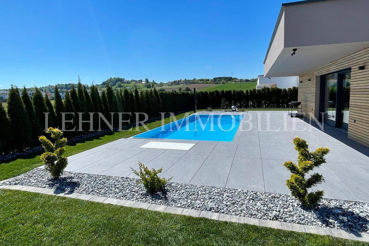 Weitläufige Poolterrasse mit Blick auf die hügelige Landschaft und gepflegte Hecke.