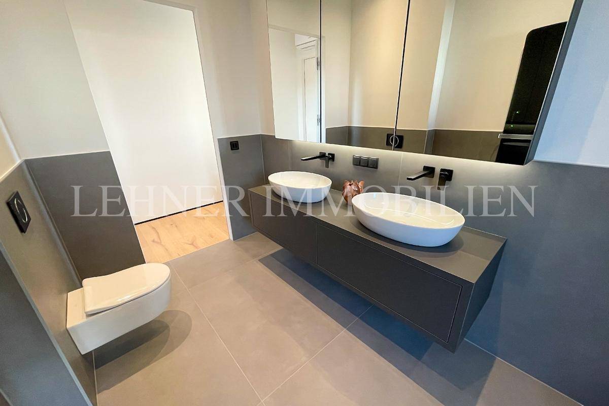 Helles Badezimmer mit Doppelwaschbecken, wandhängender Toilette und großem Spiegel.
