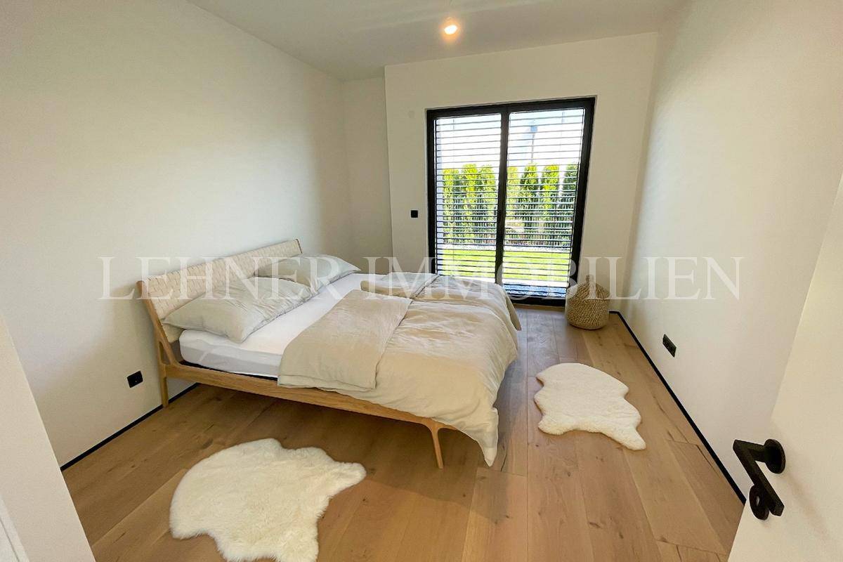 Modernes Schlafzimmer mit Holzboden und großen Fenstern, die viel Tageslicht hereinlassen.