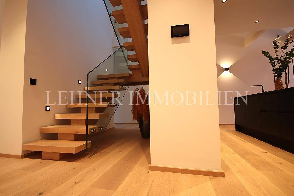 Elegante Holztreppe mit Glasgeländer und indirekter Beleuchtung, führt in die obere Etage.