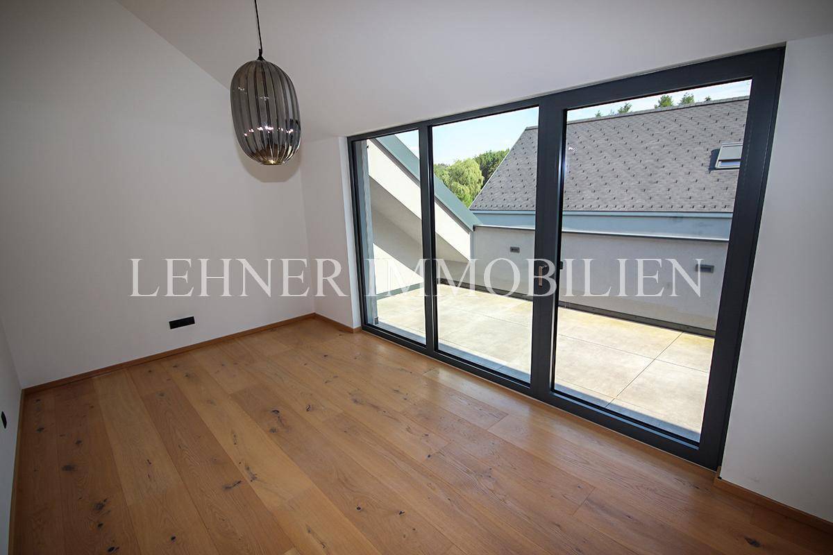 Geräumiger Raum mit Holzboden und großen Fenstern, die auf eine Dachterrasse führen.