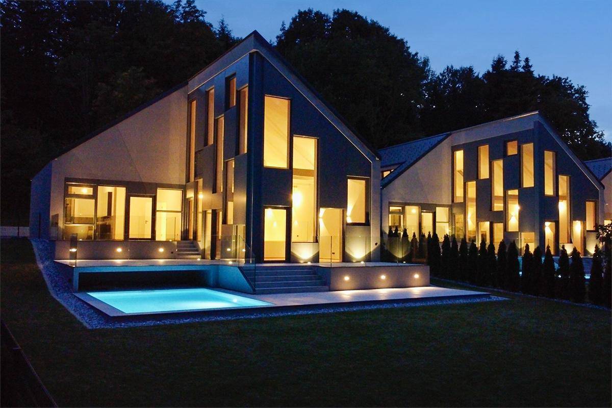 Elegante moderne Villa bei Dämmerung mit beleuchtetem Pool und gepflegtem Gartenbereich.