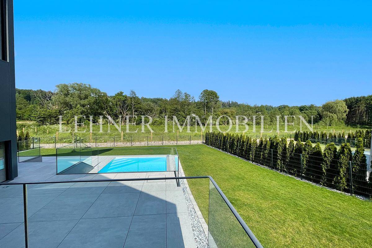 Weitläufige Terrasse mit Glasgeländer und Blick auf den Pool und die grüne Landschaft.
