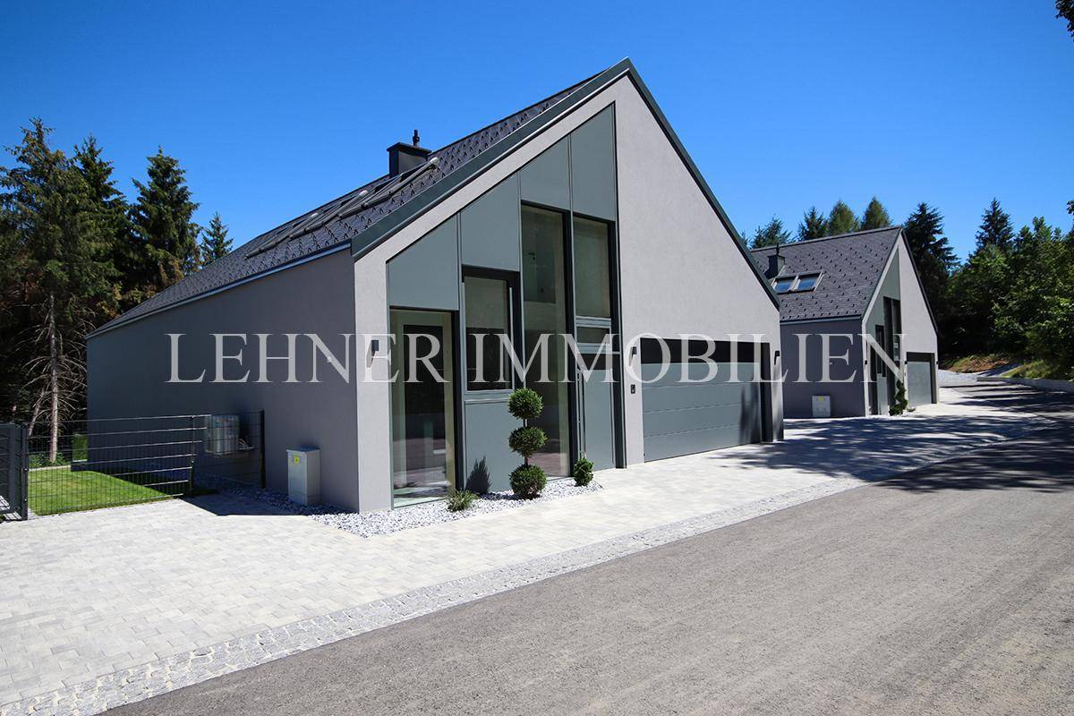 Moderne Architektur mit schräger Dachlinie und gepflasterter Auffahrt, umgeben von Bäumen.