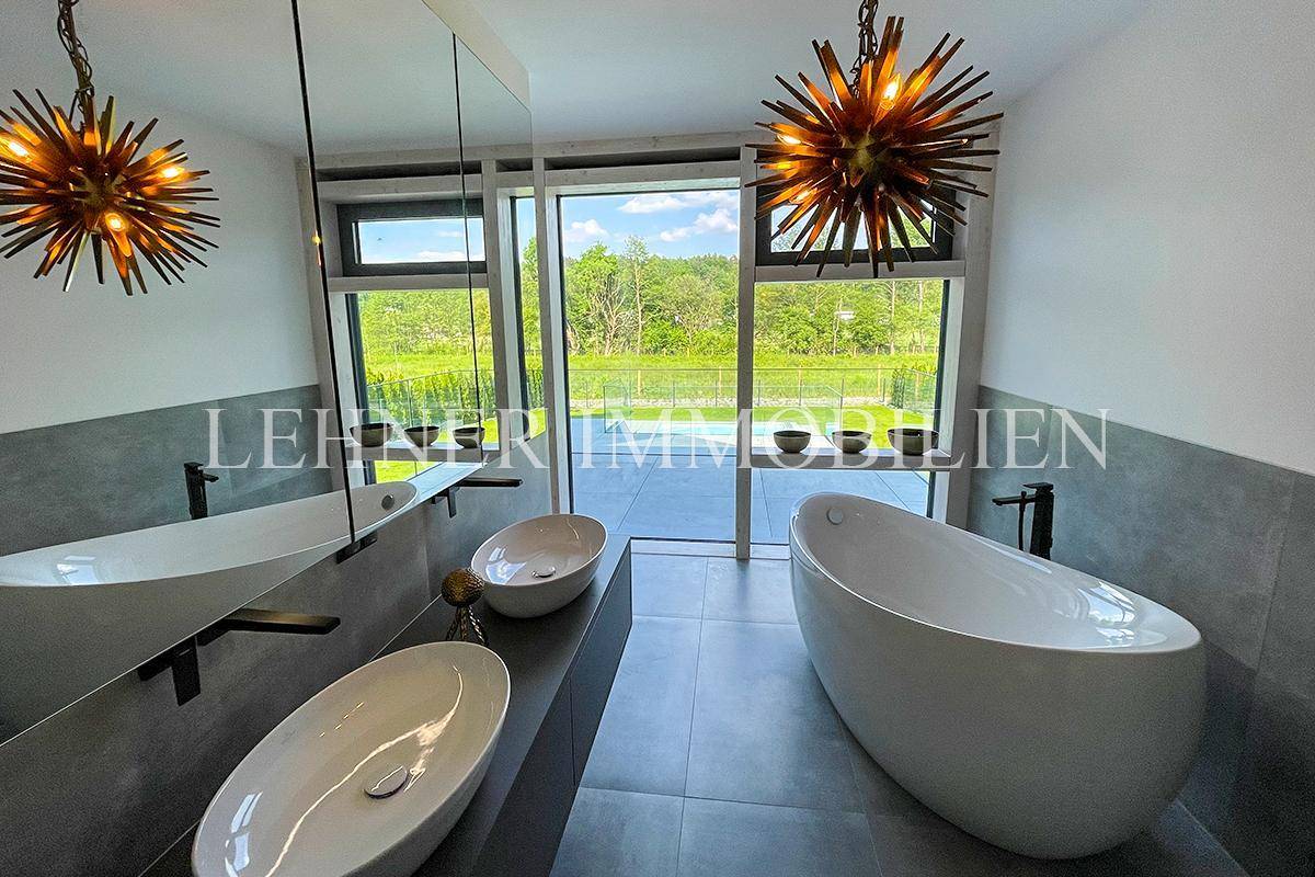 Modernes Badezimmer mit freistehender Badewanne, Doppelwaschbecken und großen Fenstern.