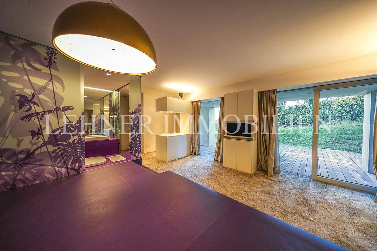Helles Schlafzimmer mit lila Akzenten, Teppichboden und Blick in den Garten.