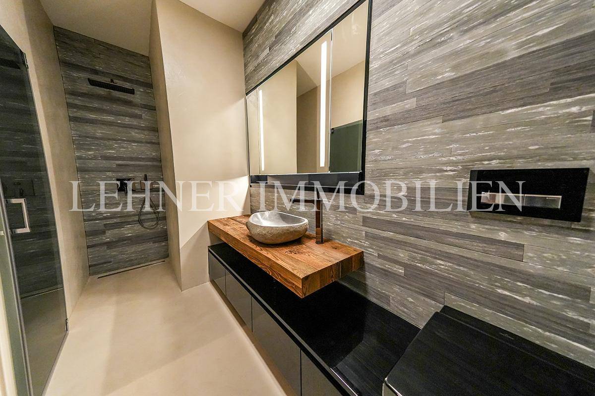 Modernes Badezimmer mit Steinwaschbecken, Holzplatte und grauen Wandfliesen.