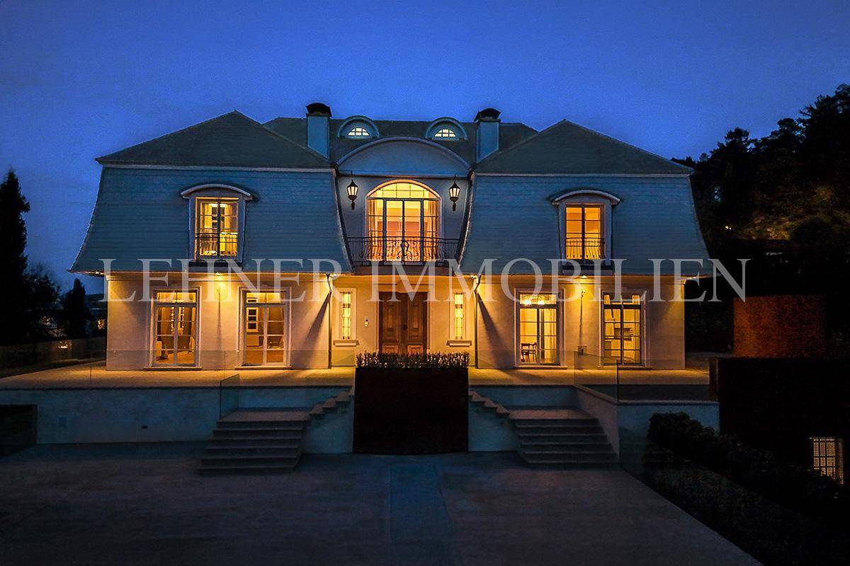 Beleuchteter Eingangsbereich der Villa bei Nacht mit klassischer Architektur und Balkon.
