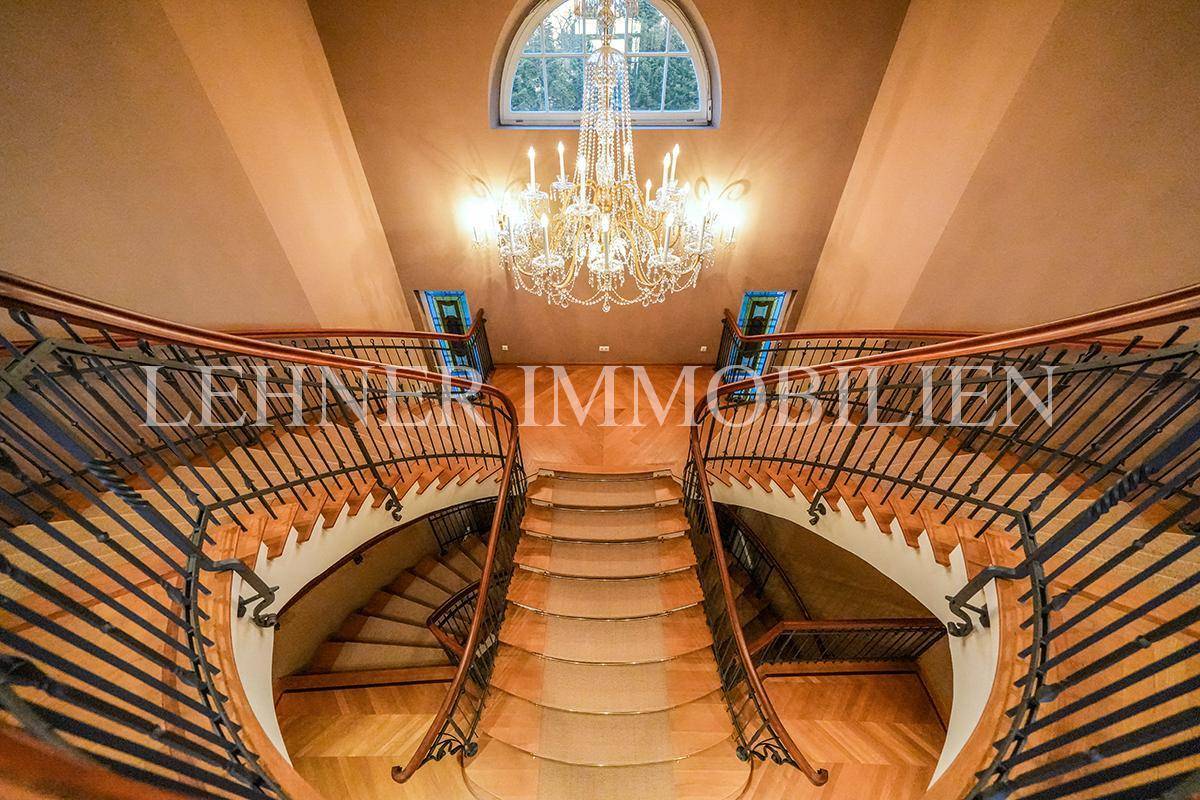 Beeindruckendes Treppenhaus mit geschwungener Doppeltreppe, Kronleuchter und Bogenfenster.