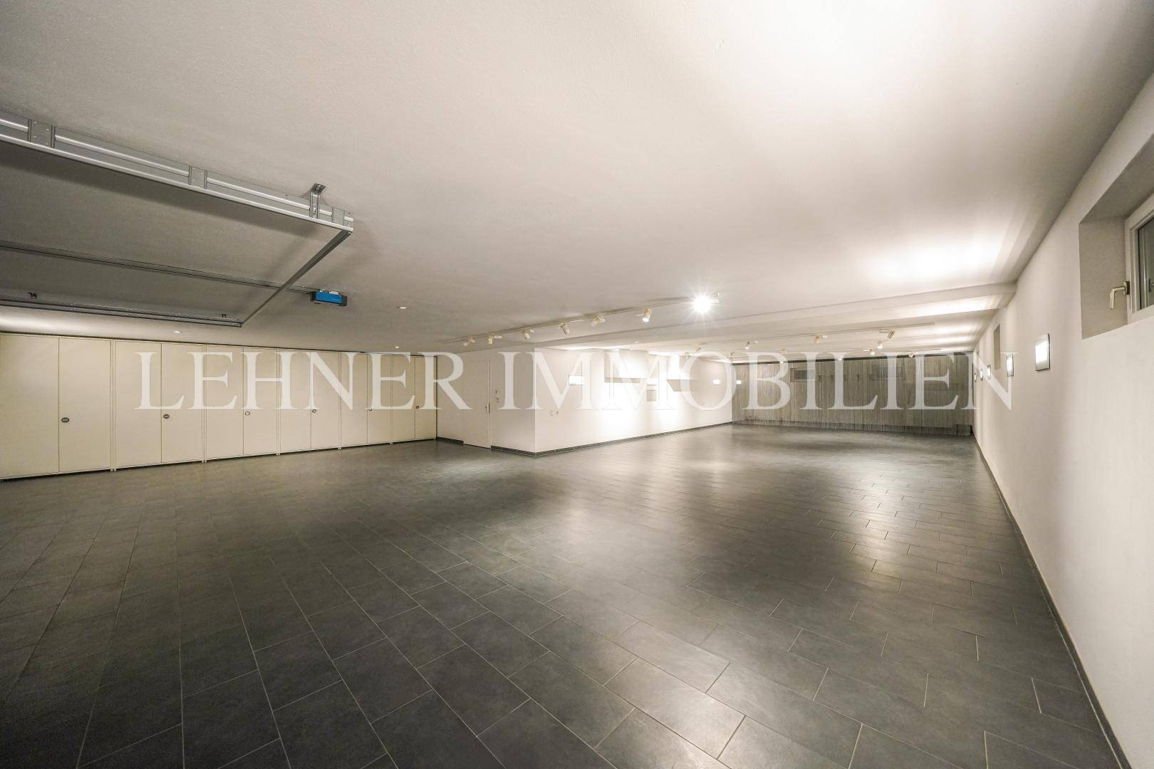 Große Tiefgarage mit Fliesenboden, Rolltor und integrierten Wandschränken.