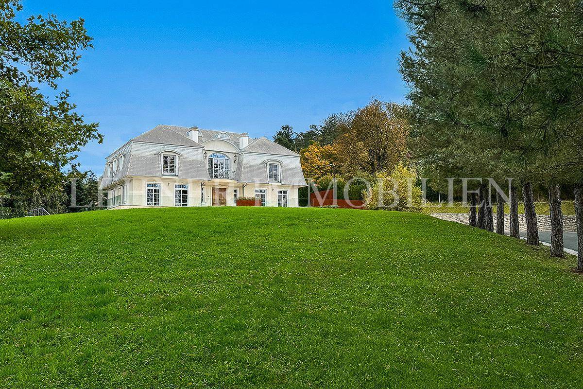 Elegante Villa auf einem Hügel mit weitläufigem, gepflegtem Rasen und altem Baumbestand.