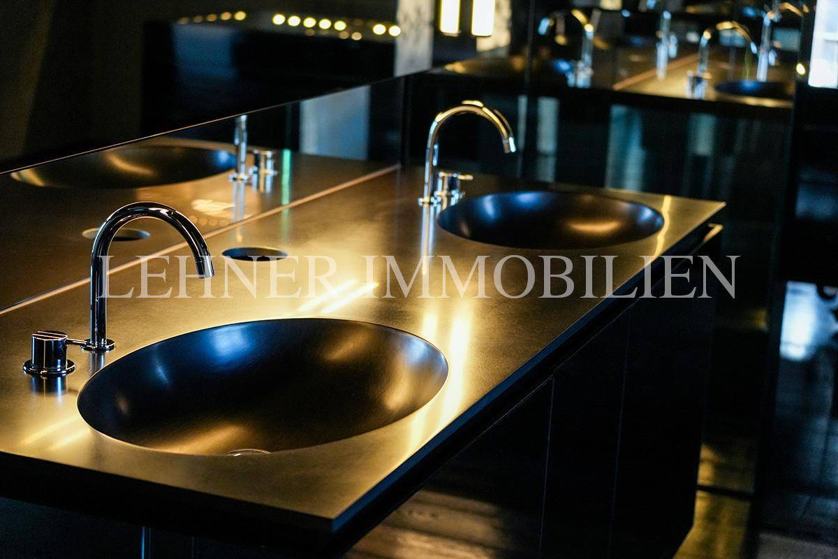 Nahaufnahme der stilvollen Doppelwaschbecken mit glänzenden Armaturen in dunklem Ambiente.