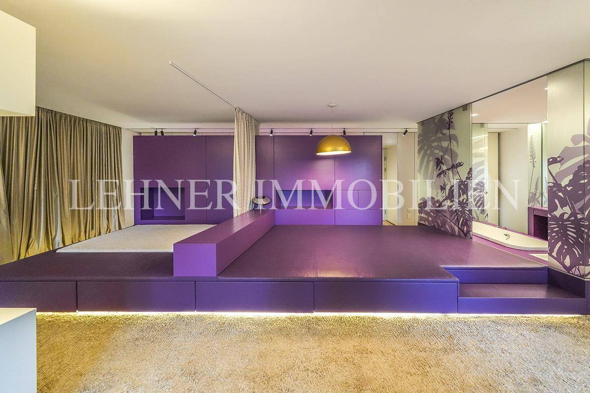 Geräumiges Schlafzimmer mit lila Podest, Teppichboden und integriertem Badezimmerbereich.