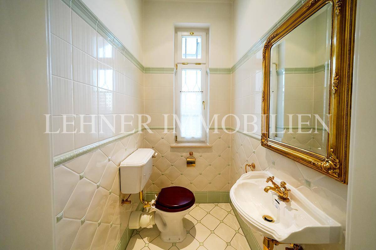 Klassisches Gäste-WC mit hellen Fliesen, goldenen Armaturen und Fenster.