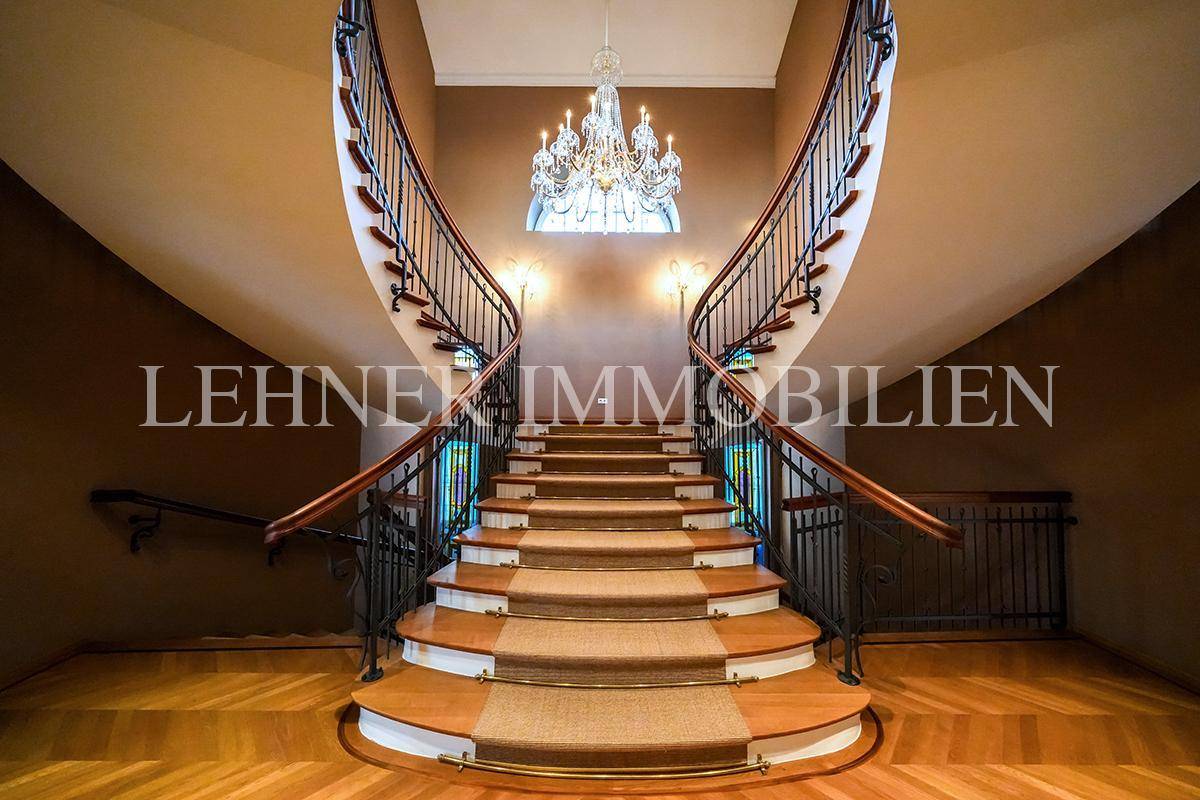 Elegantes Treppenhaus mit geschwungener Doppeltreppe, Teppichläufer und opulentem Kronleuchter.
