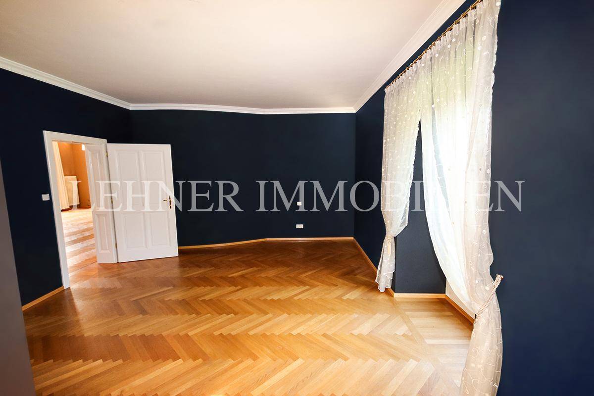 Schlafzimmer mit dunklen Wänden, Fischgrätparkett und großen Fenstern.