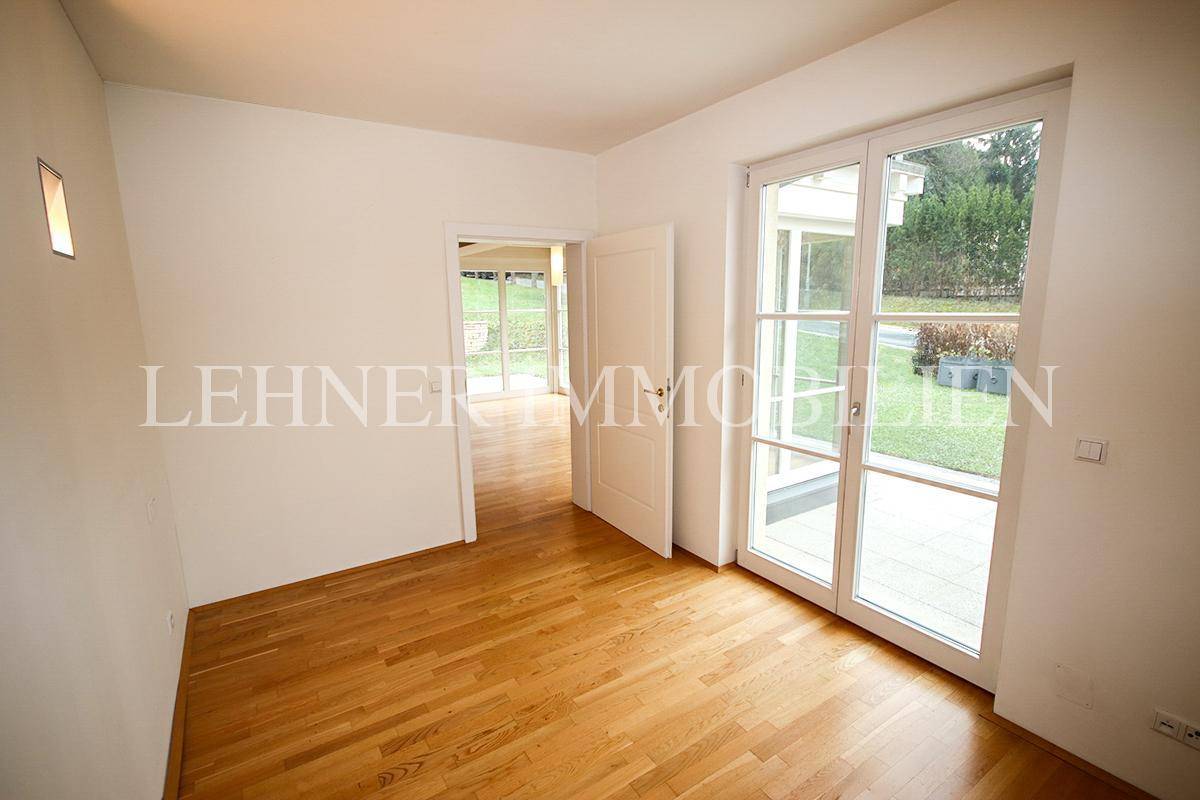 Helles Schlafzimmer mit Parkettboden, großen Fenstern und Zugang zum Garten.