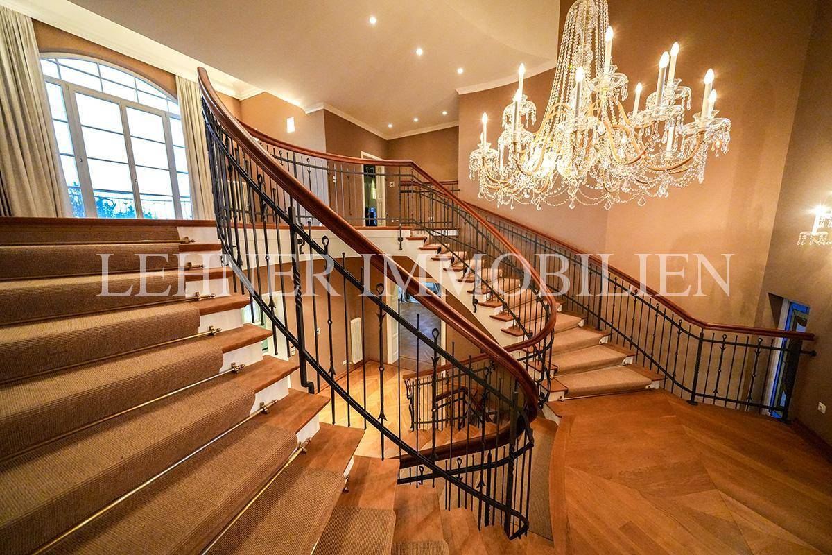 Elegantes Treppenhaus mit geschwungener Treppe, schmiedeeisernem Geländer und Kronleuchter.