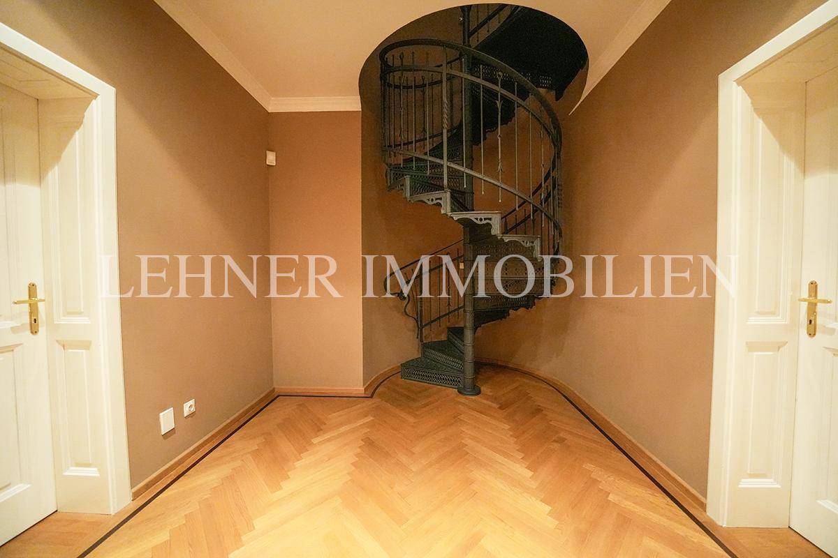 Flur mit Fischgrätparkett und eleganter Wendeltreppe aus Metall.