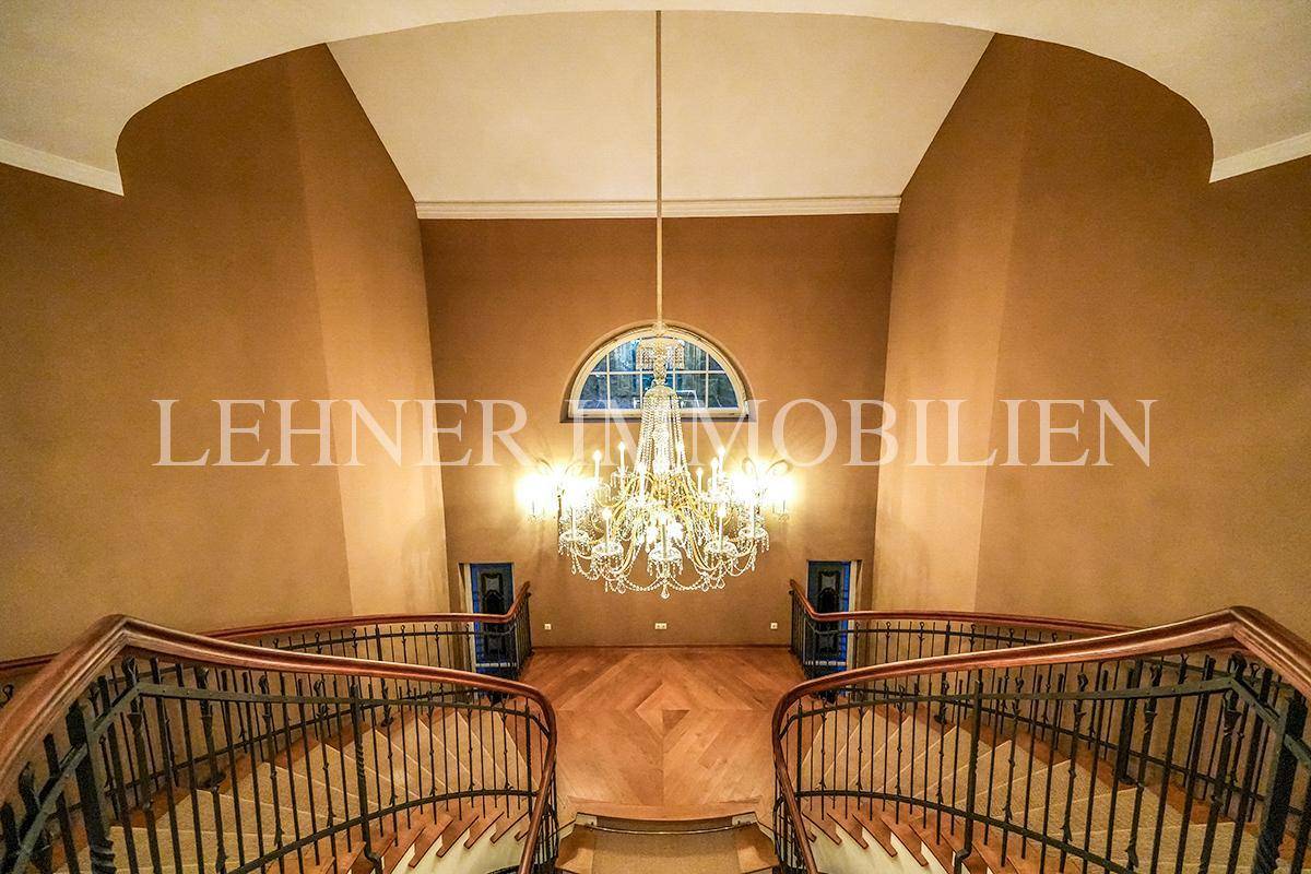 Symmetrischer Blick auf das elegante Treppenhaus mit Kronleuchter und Bogenfenster.