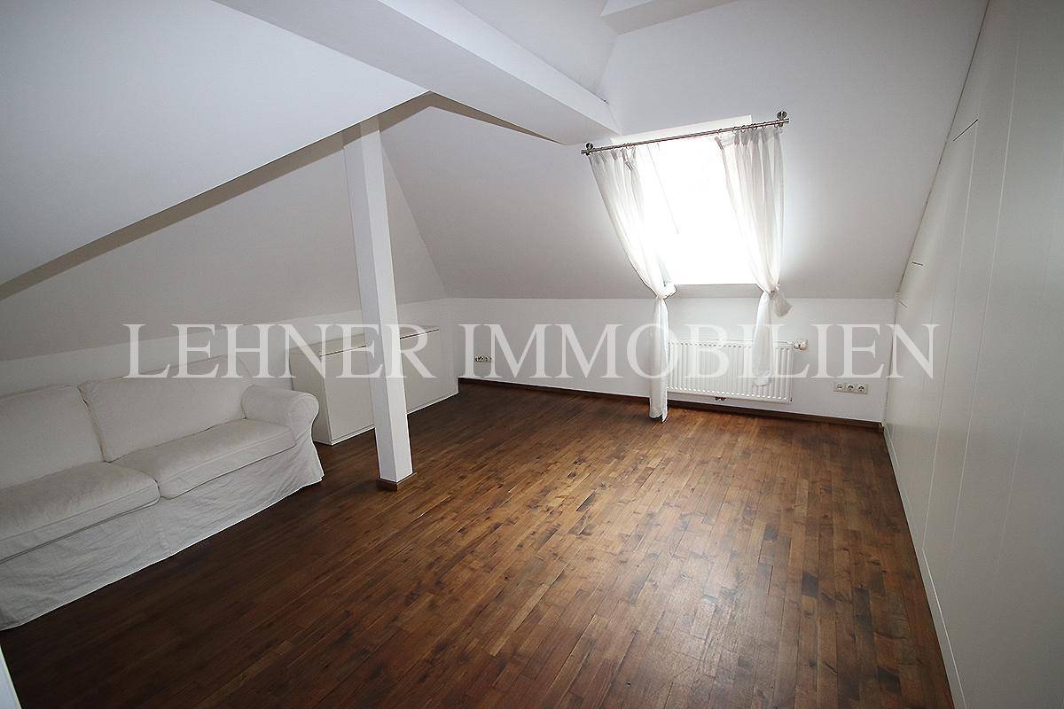 Gemütlicher Dachbodenraum mit Holzboden, weißer Couch und Fenster.