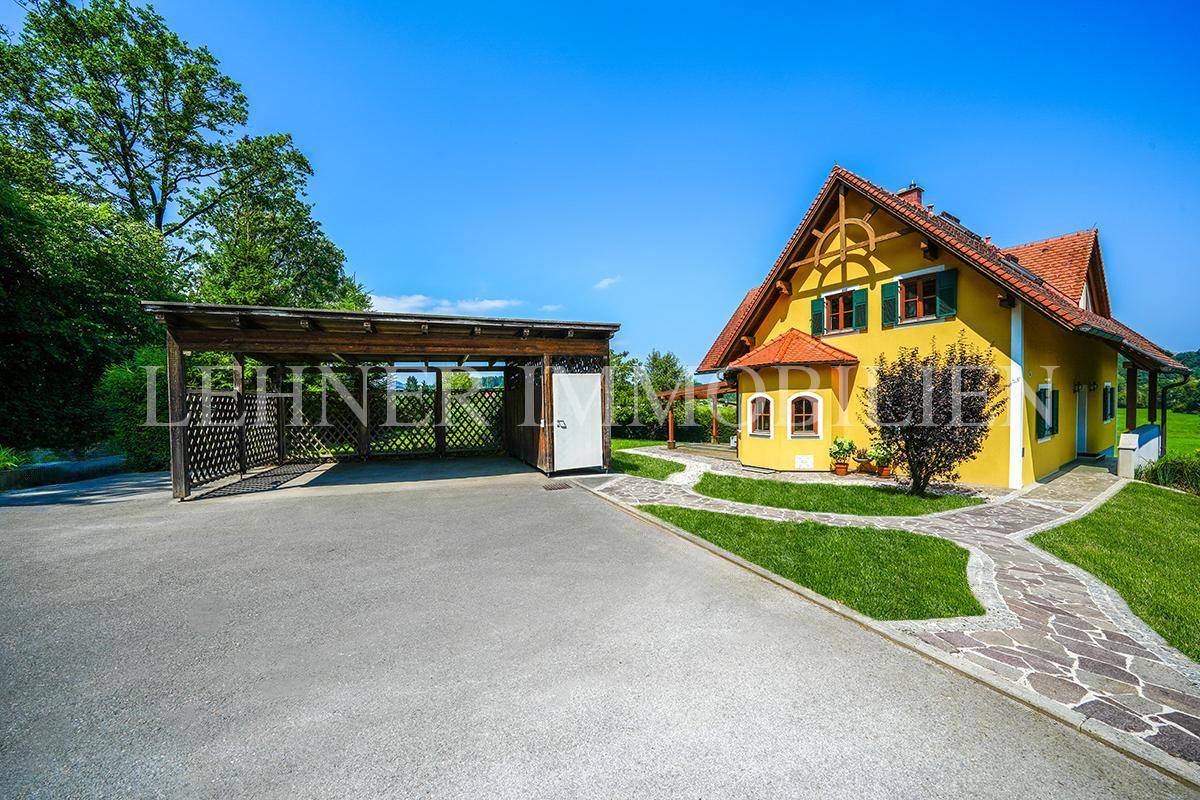 Freistehendes Haus mit gelber Fassade und großem Carport, eingebettet in eine weite grüne Landschaft.