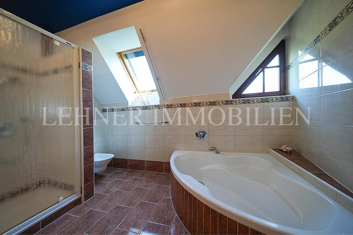 Großes Badezimmer im Dachgeschoss mit Badewanne, Dusche und Dachfenster für natürliches Licht.