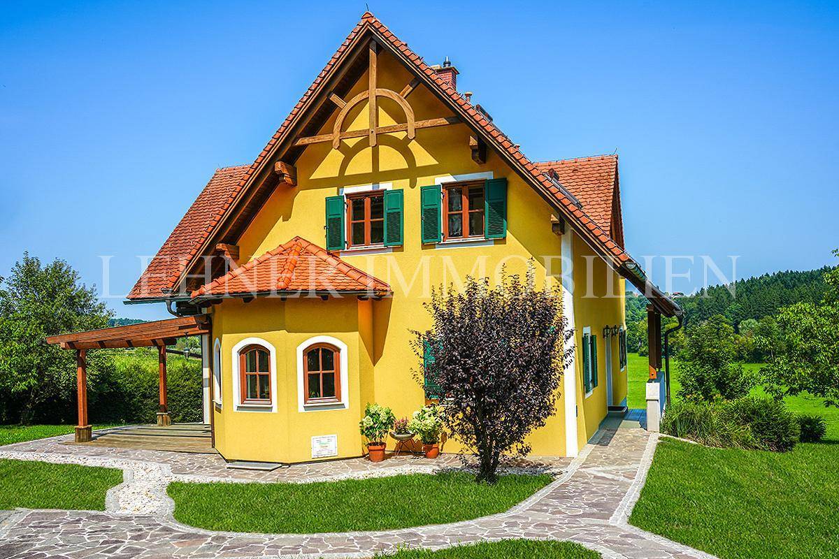 Gepflegtes Einfamilienhaus mit gelber Fassade, Ziegeldach und gepflastertem Weg, umgeben von viel Grün.