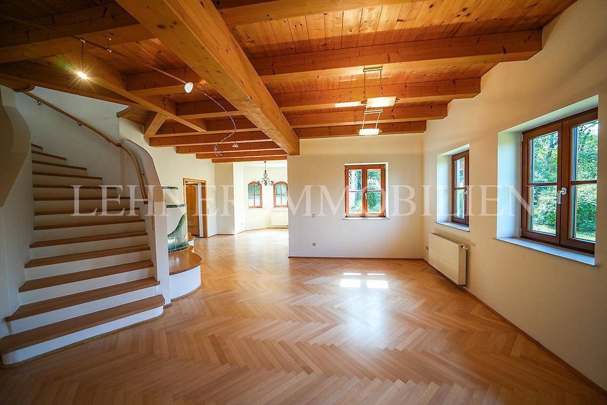 Offener Wohnbereich mit geschwungener Treppe, Fischgrätparkett und sichtbaren Holzbalken.