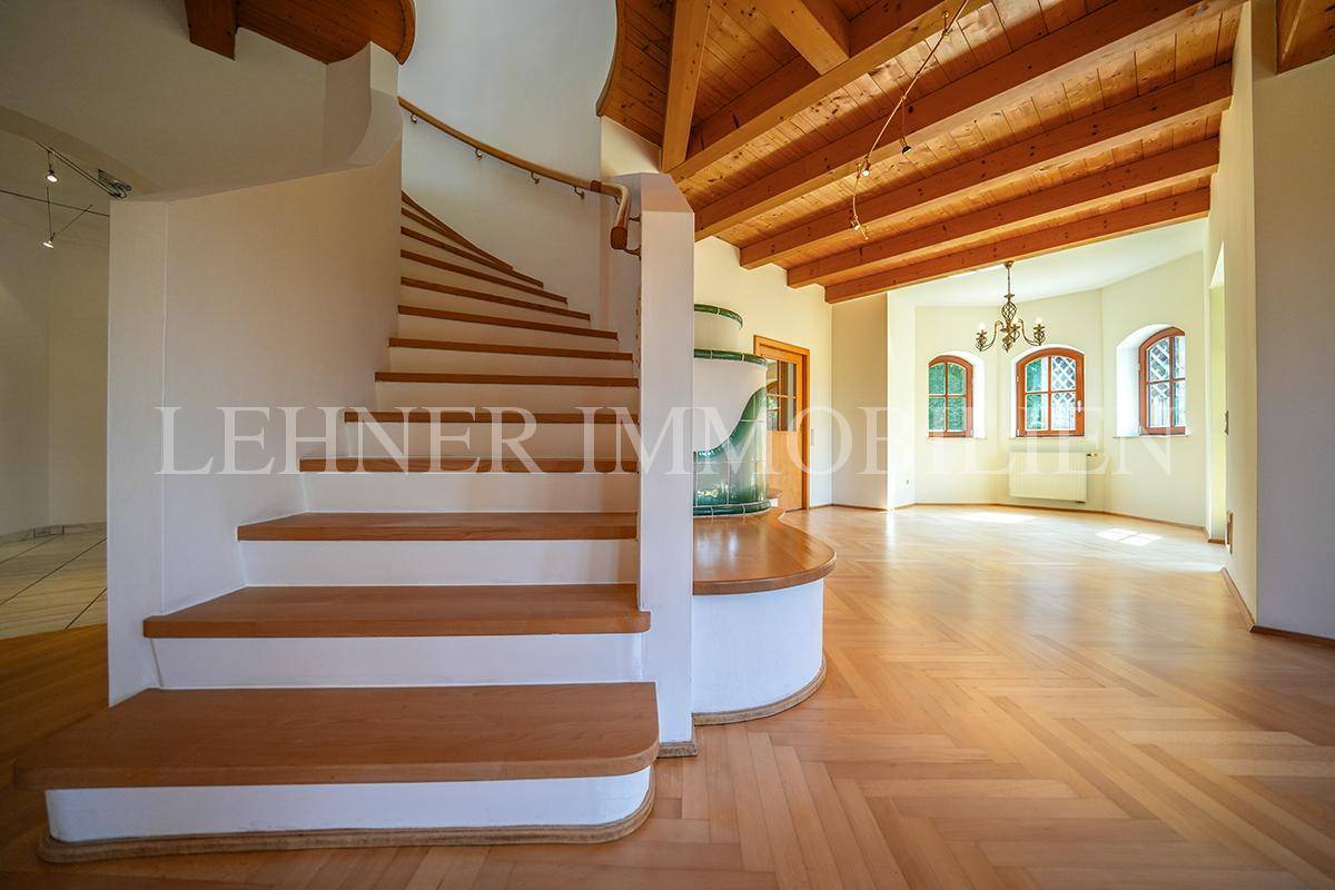 Elegante Holztreppe im offenen Wohnbereich mit Fischgrätparkett und traditionellem Kachelofen.