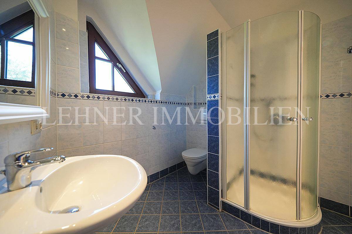 Badezimmer im Dachgeschoss mit Dusche, Waschbecken und blauen Fliesen.