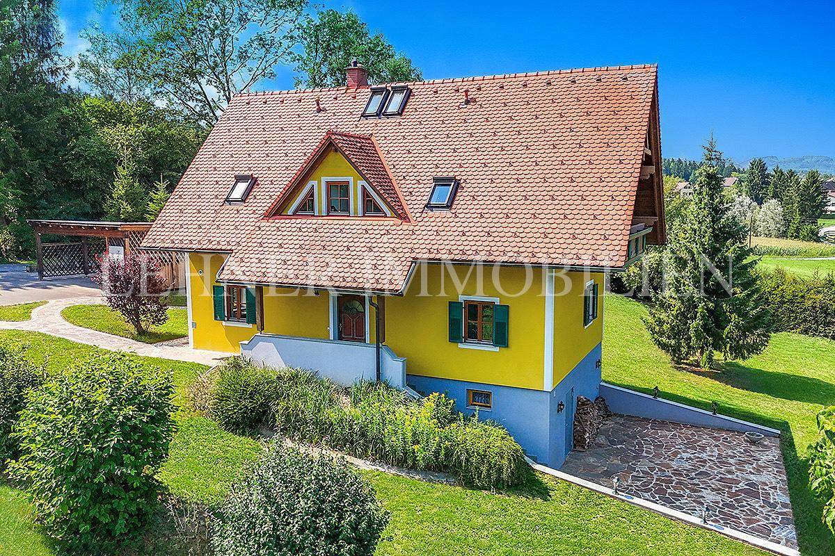 Rückansicht des Hauses mit gelber Fassade, Ziegeldach, Dachfenstern und gepflasterter Zufahrt.