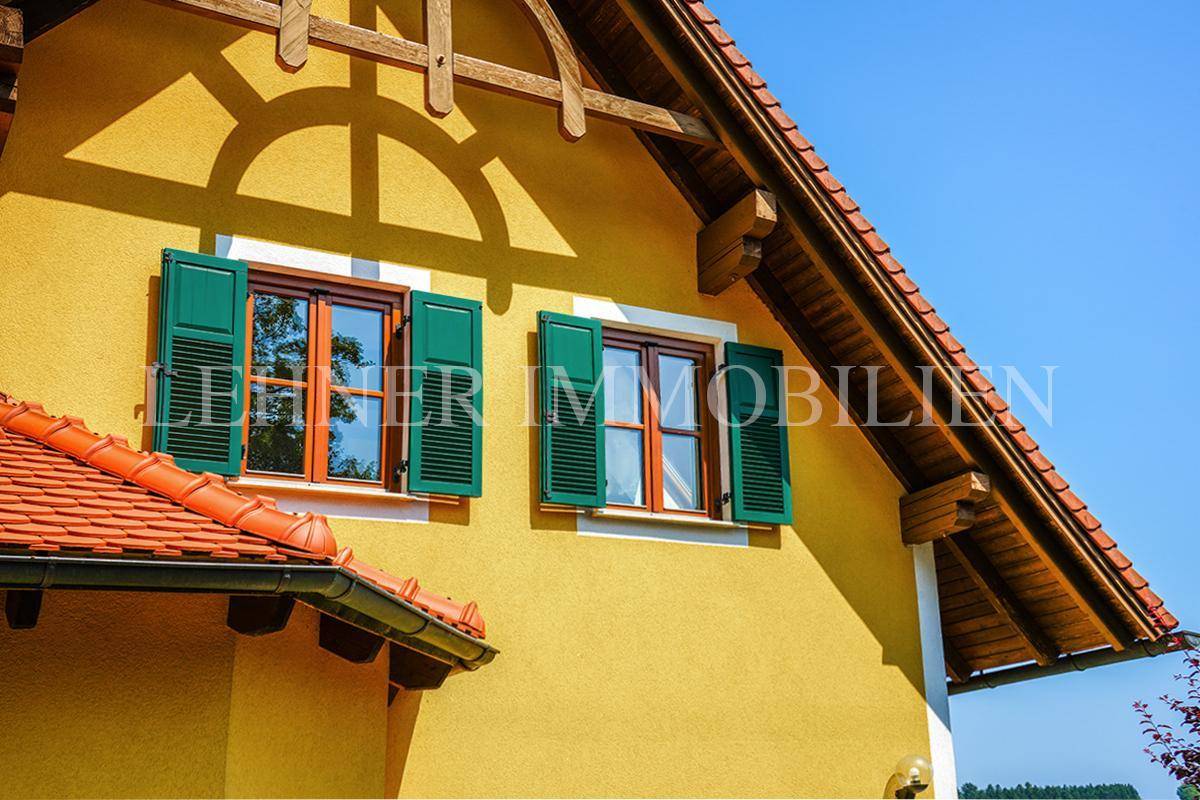 Nahaufnahme der gelben Fassade mit grünen Fensterläden und Holzbalken unter dem Dach.