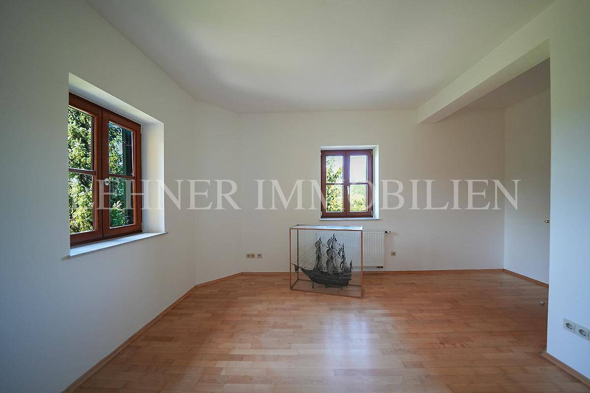 Helles Zimmer mit Holzboden und mehreren Fenstern, die viel Tageslicht hereinlassen.