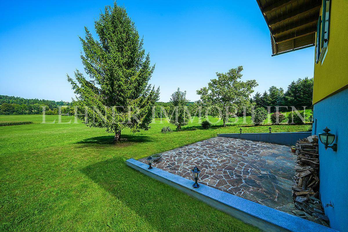 Weitläufiger Gartenbereich mit gepflegtem Rasen, hohen Bäumen und Natursteinpflasterung.