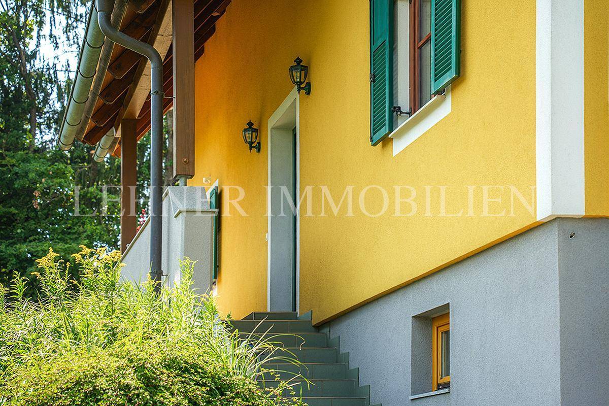Eingangsbereich des Hauses mit gelber Fassade, grünen Fensterläden und Steintreppe.